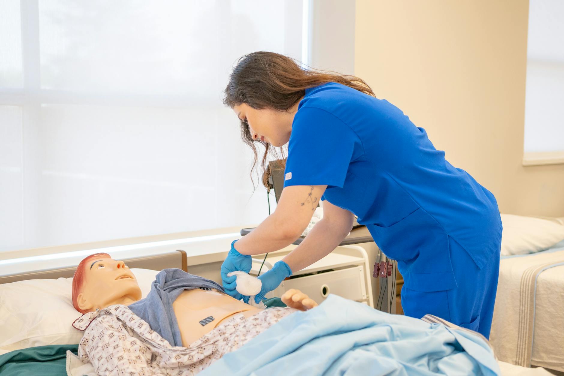 Pielęgniarka w niebieskim uniformie ćwiczy procedury na manekinie medycznym