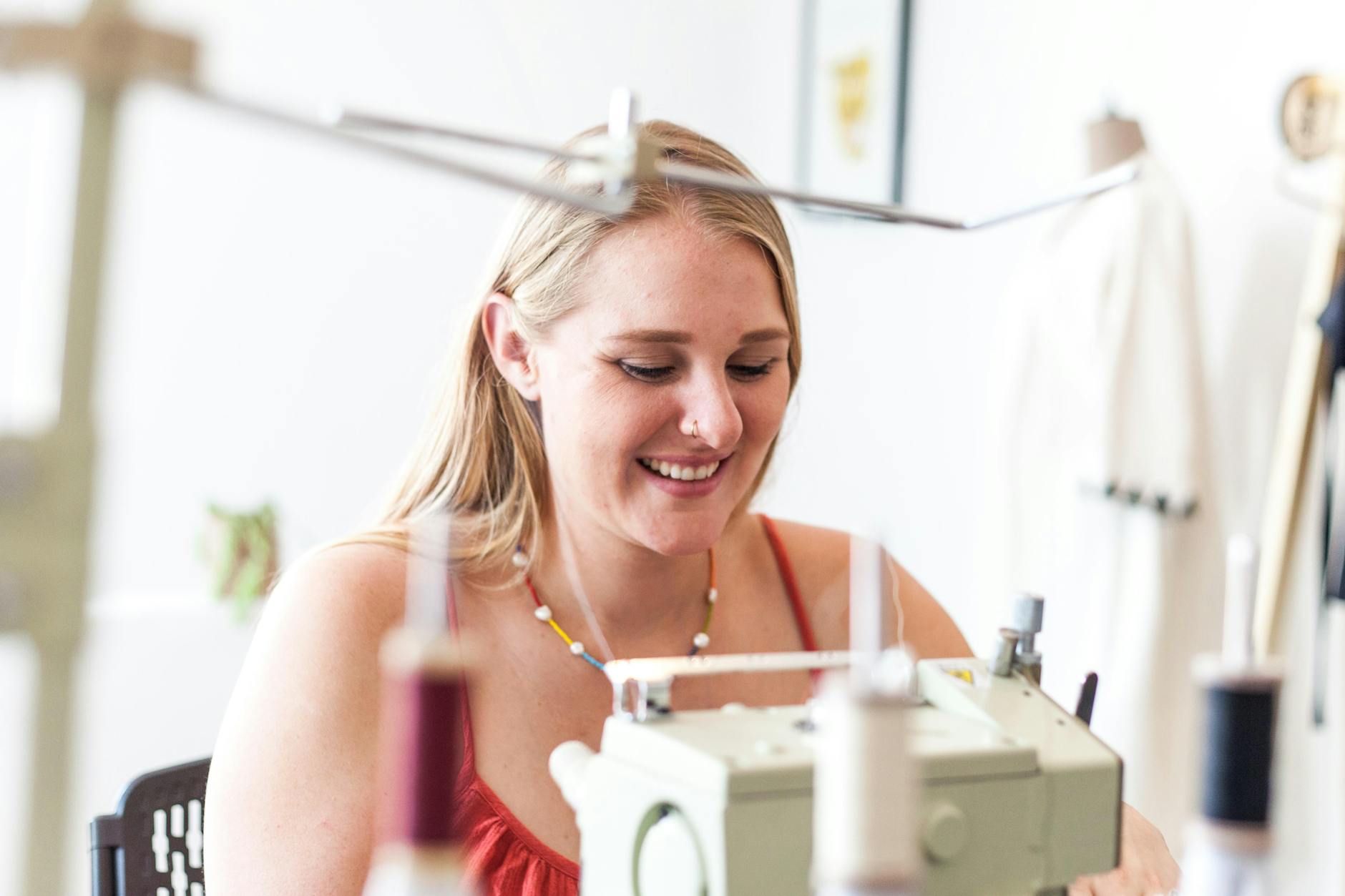 Uśmiechnięta kobieta szyje na maszynie w jasnym domowym warsztacie