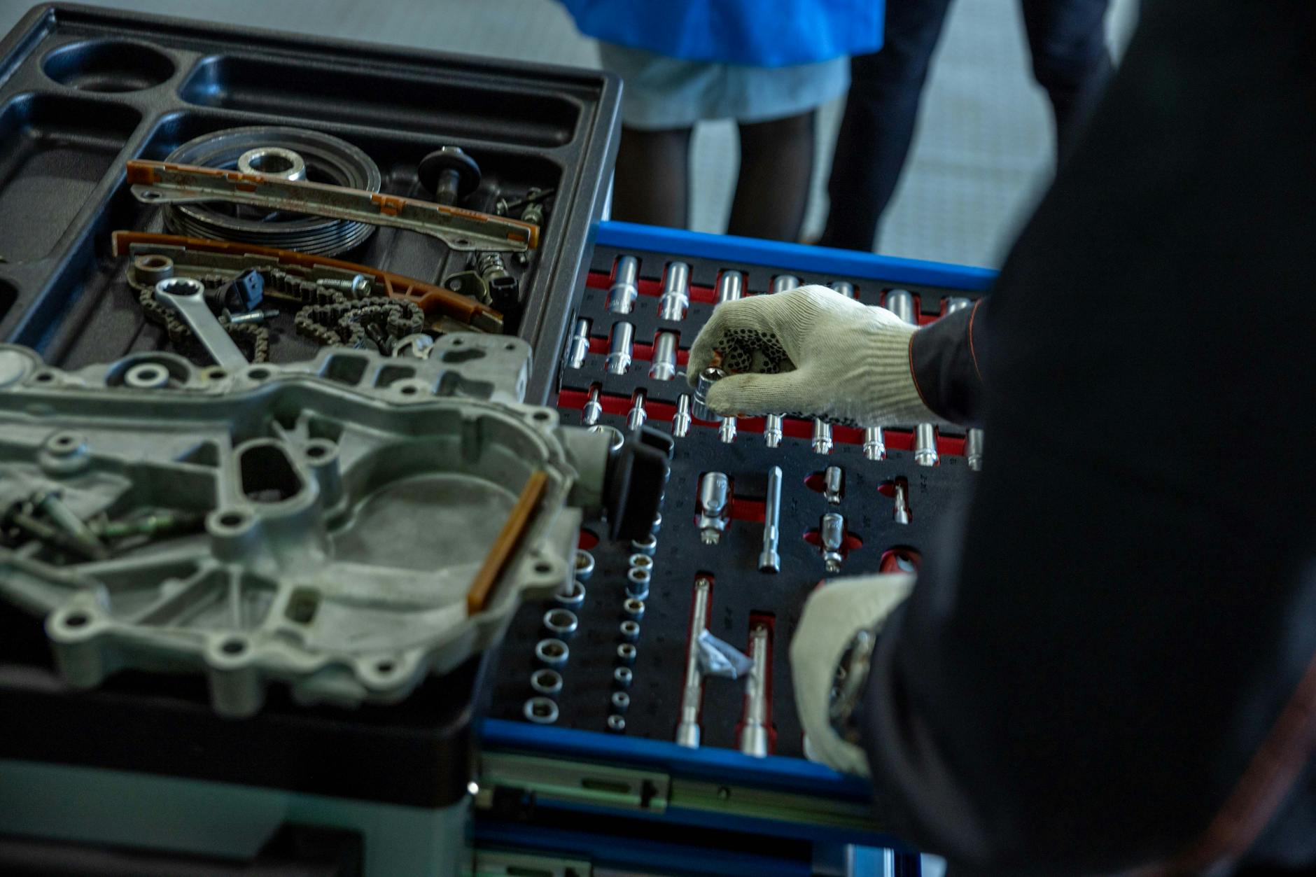 Mechanik w rękawicach porządkuje części silnika i narzędzia w warsztacie