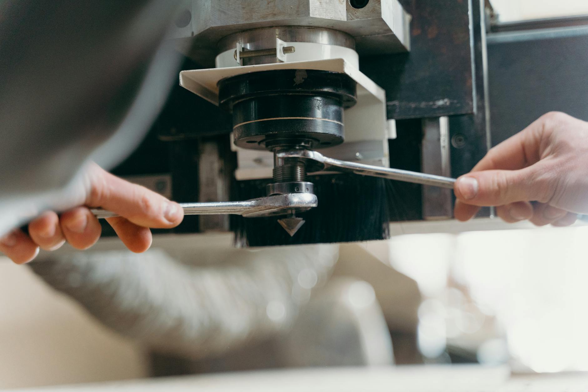 Operator reguluje maszynę CNC kluczami w hali produkcyjnej