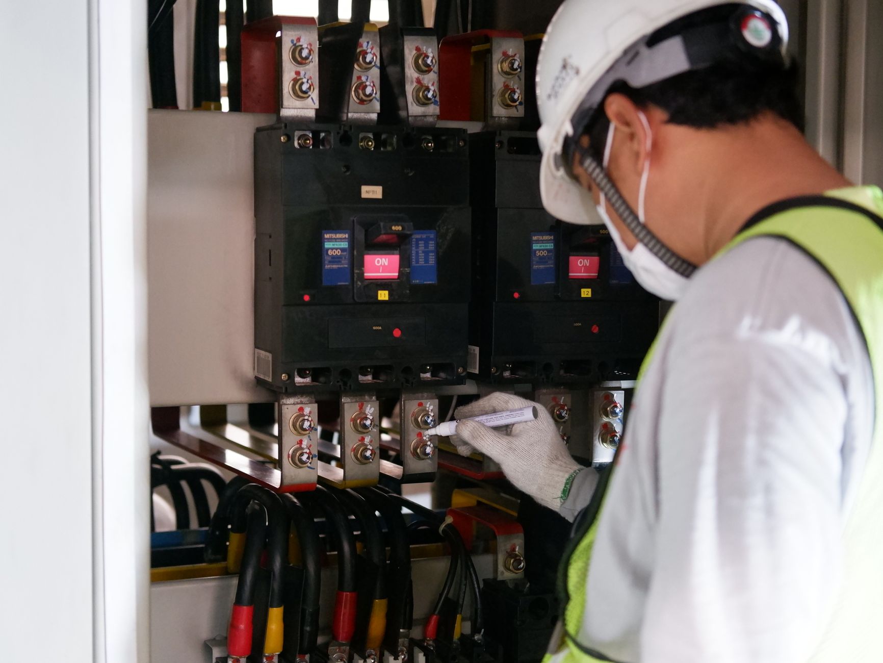 Technik w okularach ochronnych sprawdza szafę elektryczną w hali produkcyjnej